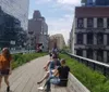 The image shows people walking and sitting along a landscaped elevated park with city buildings on each side which is reminiscent of the High Line in New York City