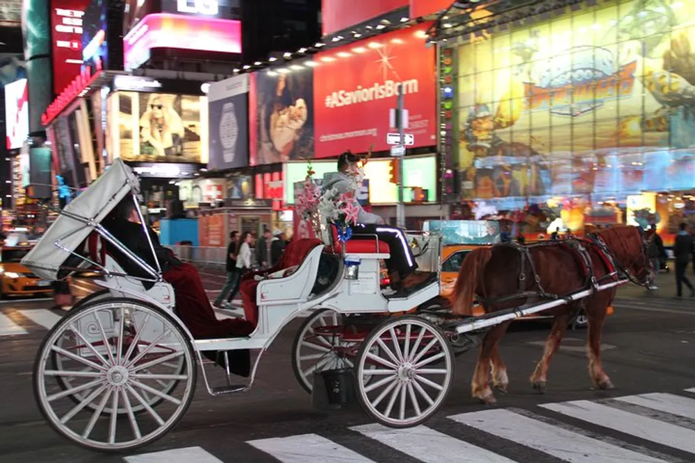 A horse-drawn carriage crosses an intersection in the brightly lit and bustling Times Square at night