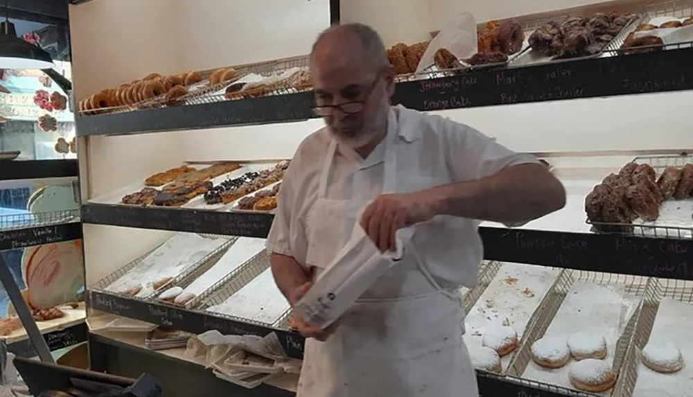 A baker is bagging pastries behind the nearly sold-out display shelves of a bakery