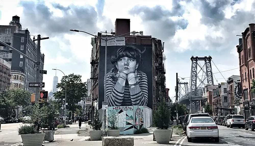 This image features a large building mural of a childs face with an urban street scene and the Williamsburg Bridge in the background