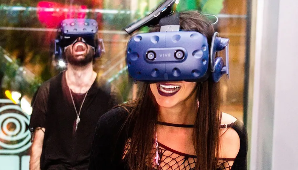 Two people are wearing VR headsets and appear to be delighted by their immersive virtual reality experience