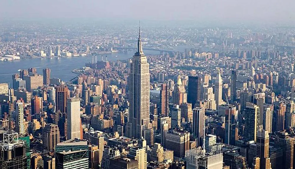 The image shows an aerial view of Manhattan with the Empire State Building prominently centered amidst the dense urban skyline