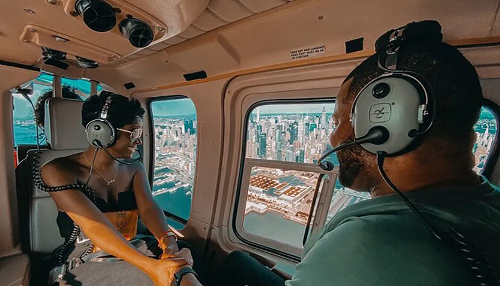 Two people are wearing headphones while enjoying a helicopter ride with a view of a city skyline