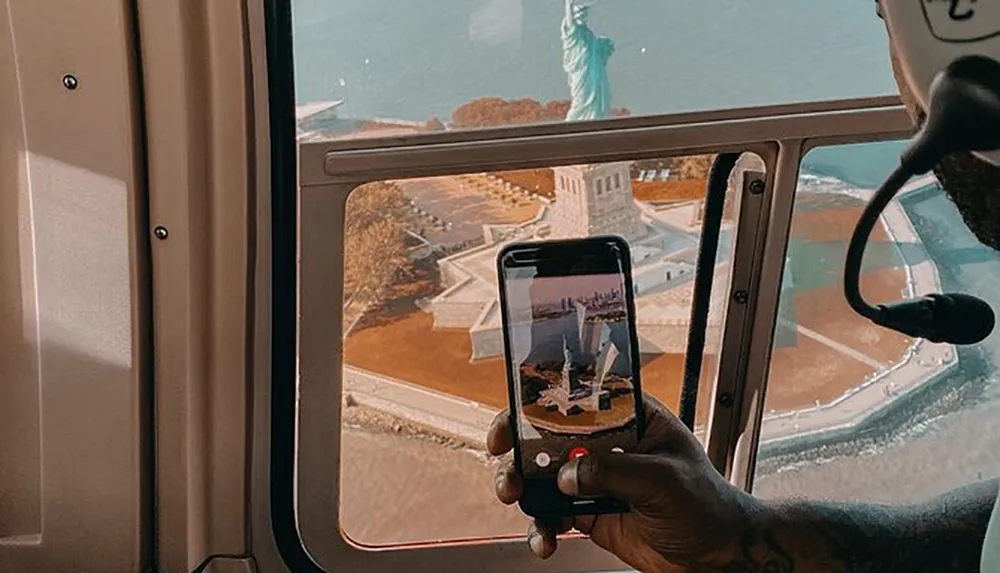 A person in a helicopter is taking a photo of the Statue of Liberty with their smartphone