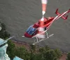 A red helicopter is flying near the Statue of Liberty