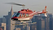A red and white helicopter is flying over the city with skyscrapers in the background.