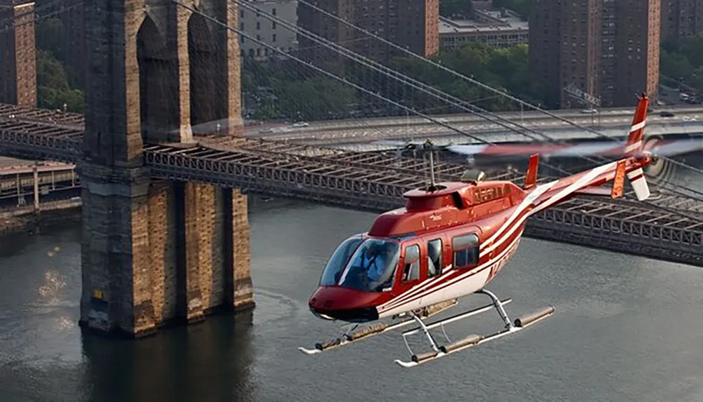 A red helicopter is flying near the Brooklyn Bridge over the East River in New York City