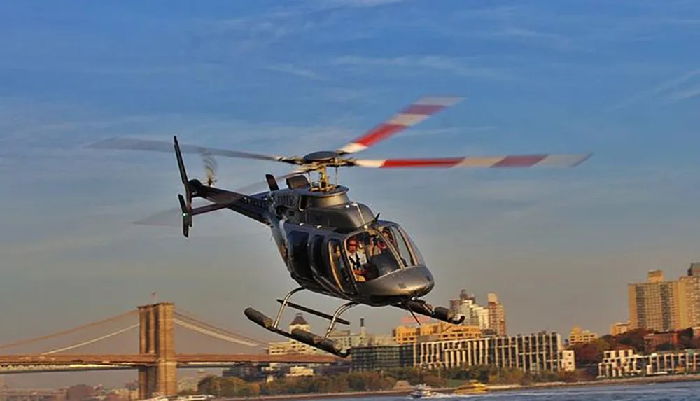 A helicopter is flying near a bridge over a cityscape during the day