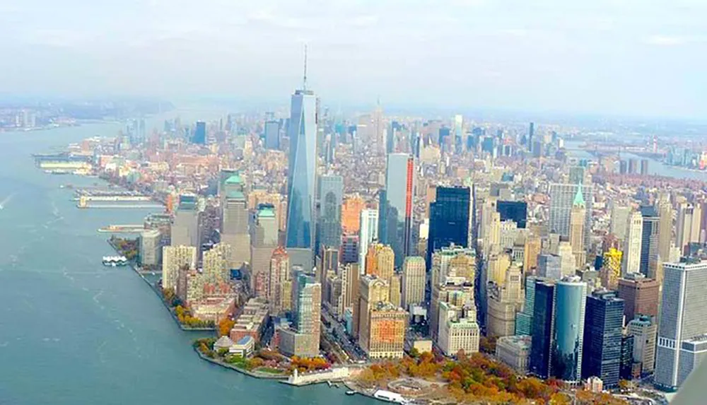 This is an aerial view of Manhattan showcasing the dense and towering skyline of New York City with the One World Trade Center prominently standing tall among the urban landscape