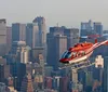 A red and white helicopter is flying over Central Park with the New York City skyline in the background