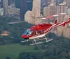 A red and white helicopter is flying over Central Park with the New York City skyline in the background