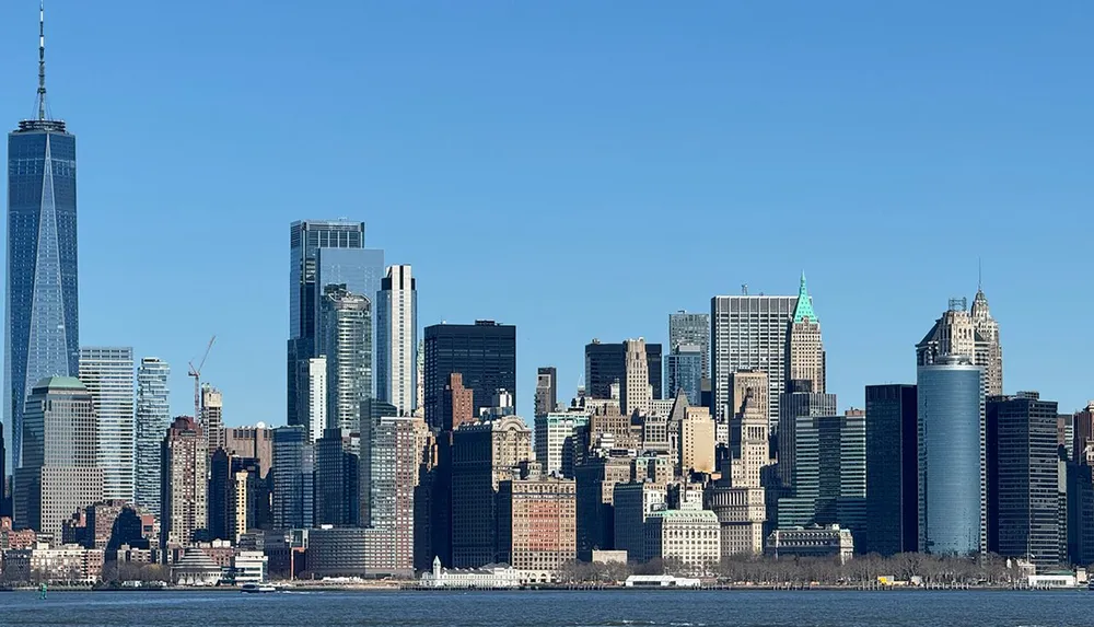 This image shows a clear daytime view of the Manhattan skyline with a variety of skyscrapers and the One World Trade Center standing prominently against a blue sky