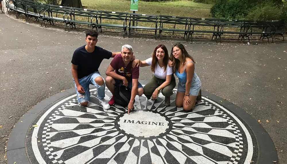 Four individuals are posing with smiles around the iconic black and white Imagine mosaic memorial in Central Park