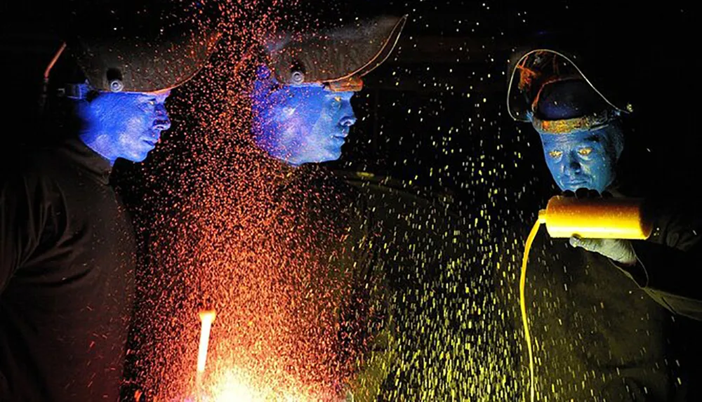 Two individuals with their faces illuminated in blue are performing with sparks flying around them creating a visually striking effect