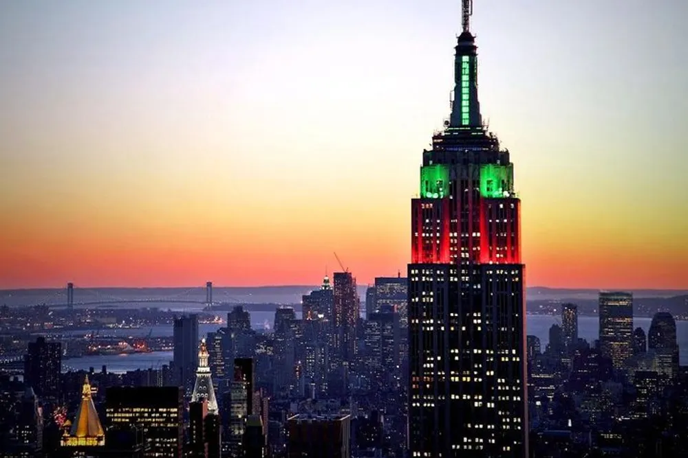 The image features the Empire State Building illuminated in green and red against the backdrop of a sunset-drenched New York City skyline