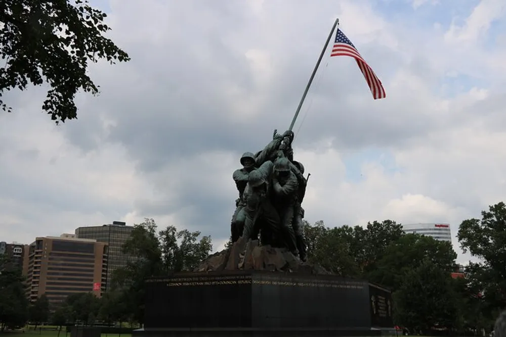 The image shows the Marine Corps War Memorial also known as the Iwo Jima Memorial depicting the iconic flag raising on Mount Suribachi with the American flag waving above the statue under a cloudy sky