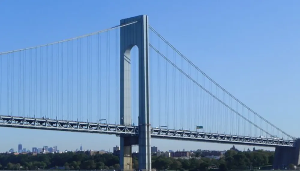 The image features a clear view of a large suspension bridge spanning over a waterway with a city skyline in the background against a blue sky