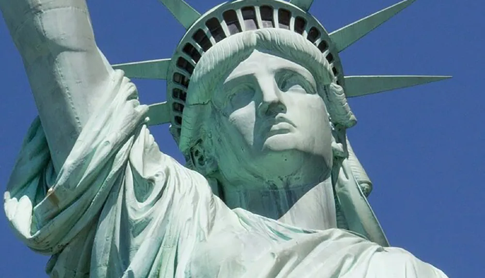 The image shows a close-up view of the Statue of Liberty against a clear blue sky
