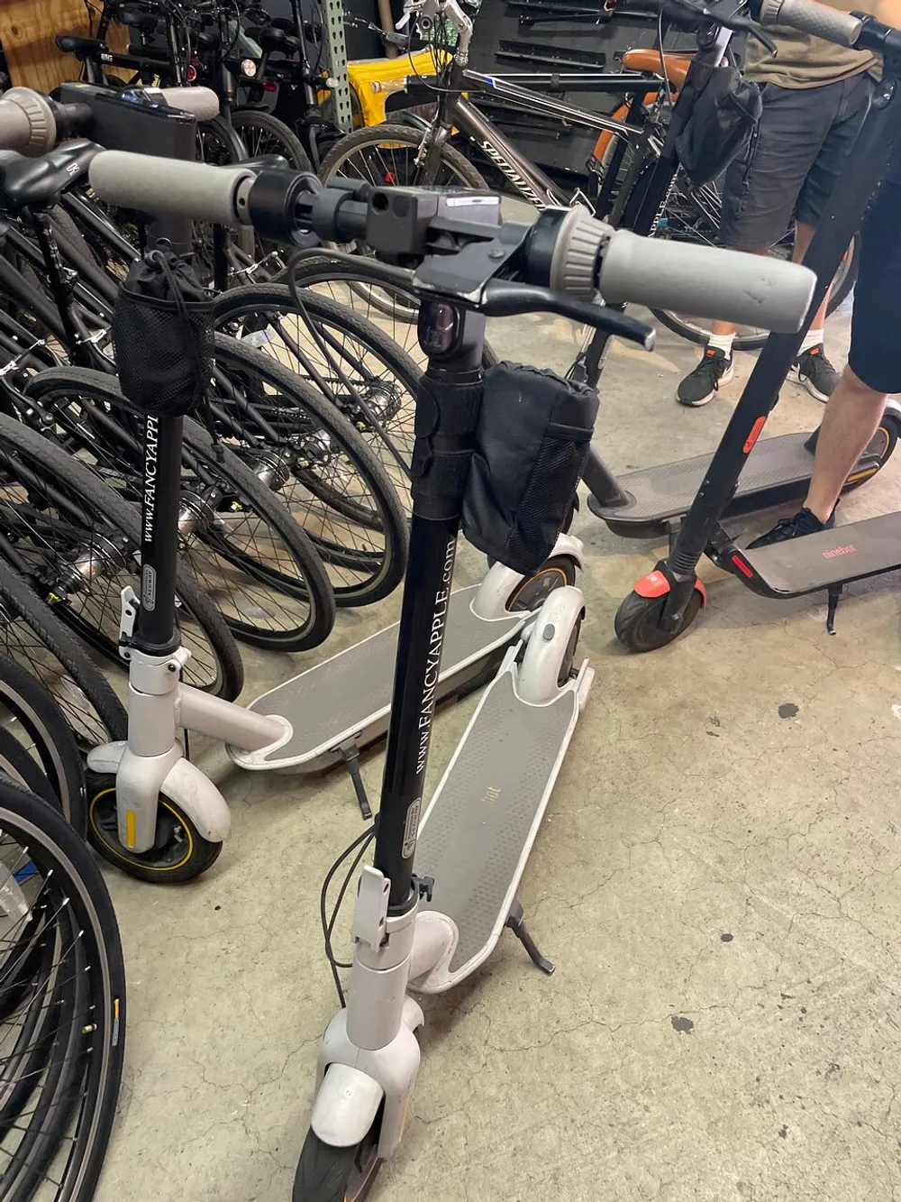 The image shows an urban scene with electric scooters and bicycles closely packed together possibly in a rental shop or parking area