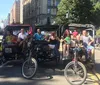 A group of smiling people is enjoying a ride in pedicabs on a sunny city street