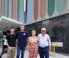 Two younger men and an older couple pose for a photo on a city sidewalk with the entrance of The Greater Refuge Temple building as their backdrop