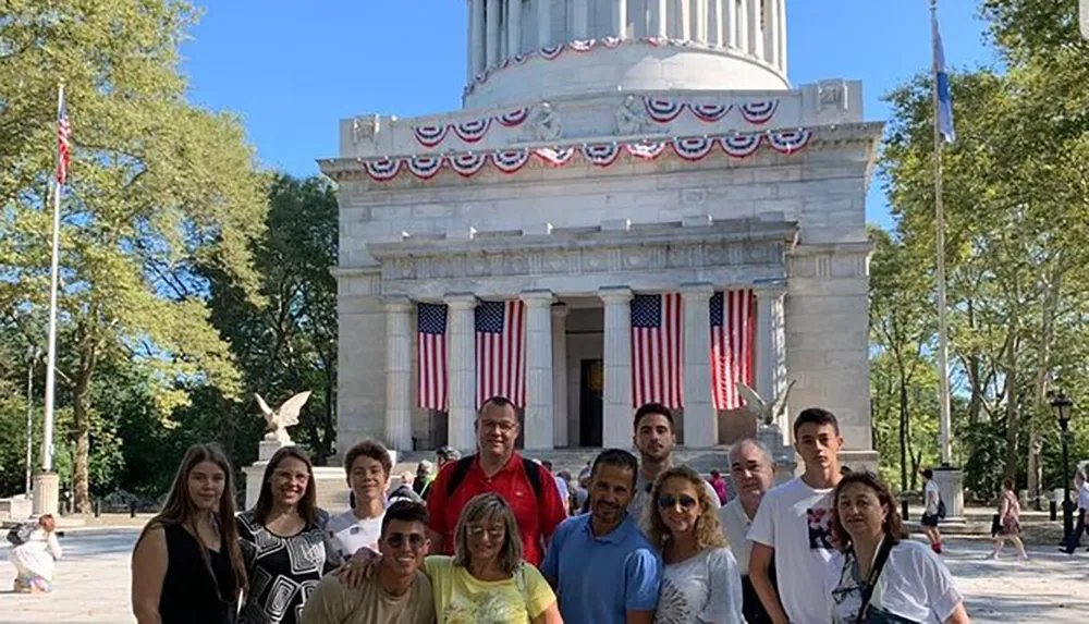 A group of people are posing for a photo in front of a neoclassical monument adorned with American flags