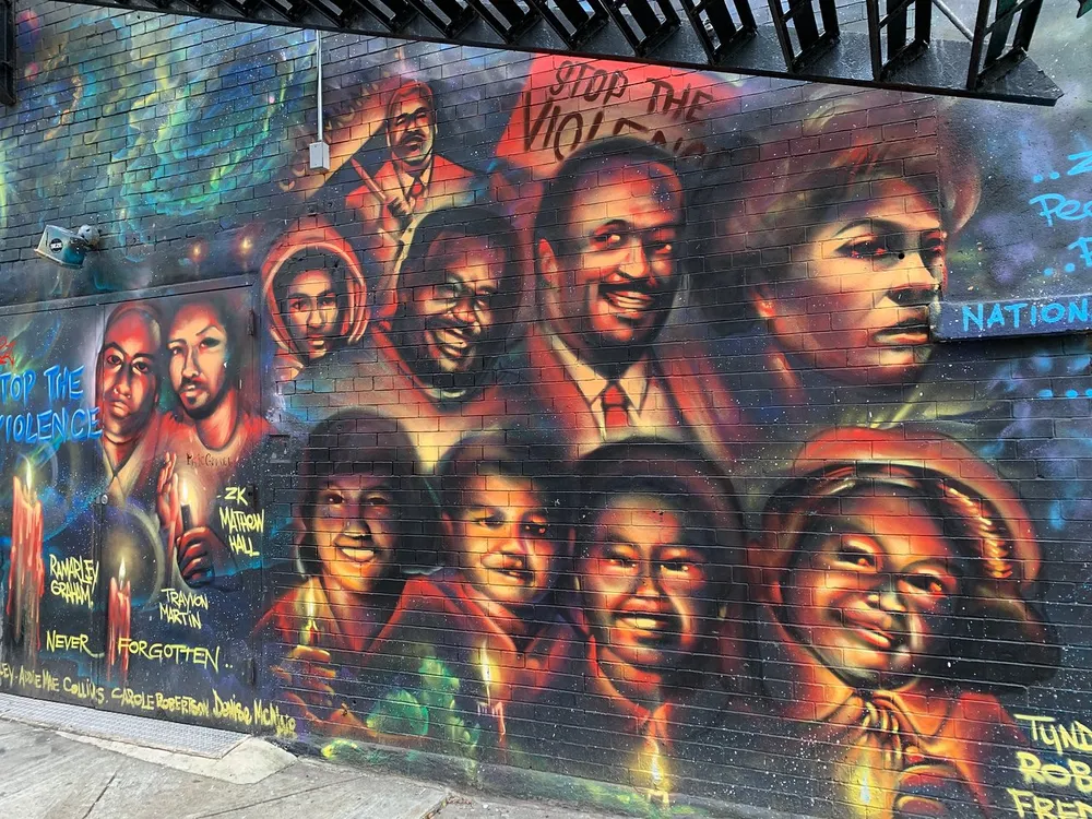 The image shows a vibrant street mural dedicated to anti-violence with the message Stop the Violence prominently featured alongside painted portraits of individuals and memorial inscriptions