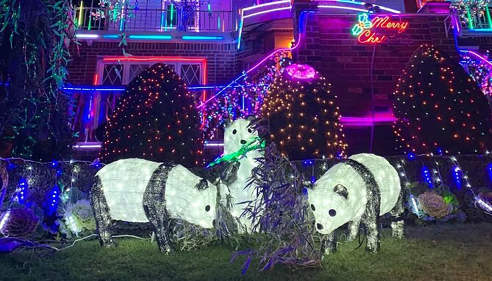 The image shows a festive outdoor Christmas decoration with illuminated wireframe polar bears and trees and a neon sign that says Merry Christmas adorning the exterior of a brick house