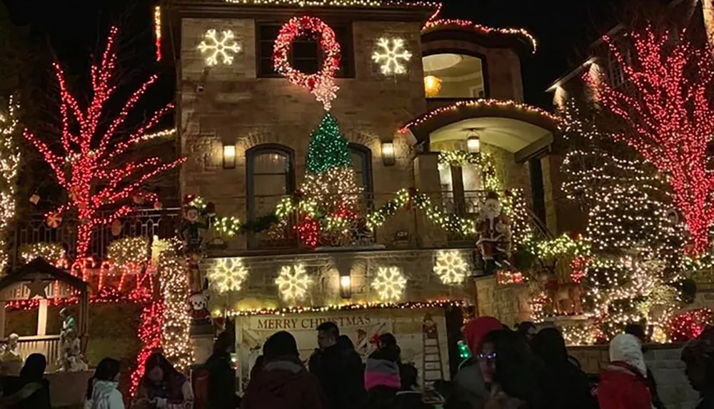 A house adorned with an elaborate display of colorful Christmas lights and decorations surrounded by a crowd of people enjoying the festive scene