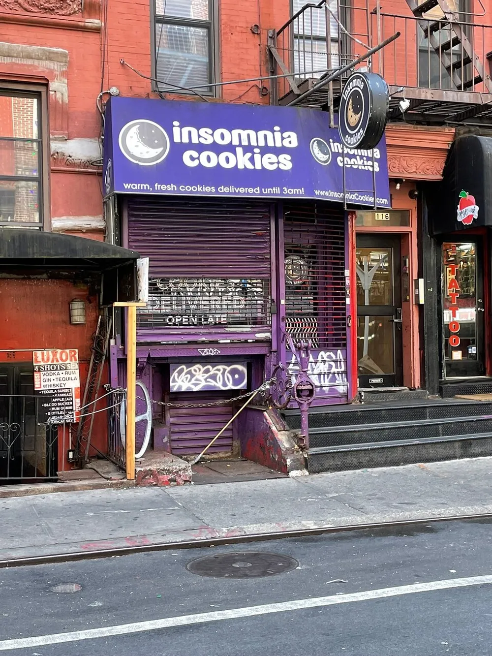 The image shows the storefront of Insomnia Cookies with its distinctive purple awning and signage advertising warm fresh cookies delivered until 3 am