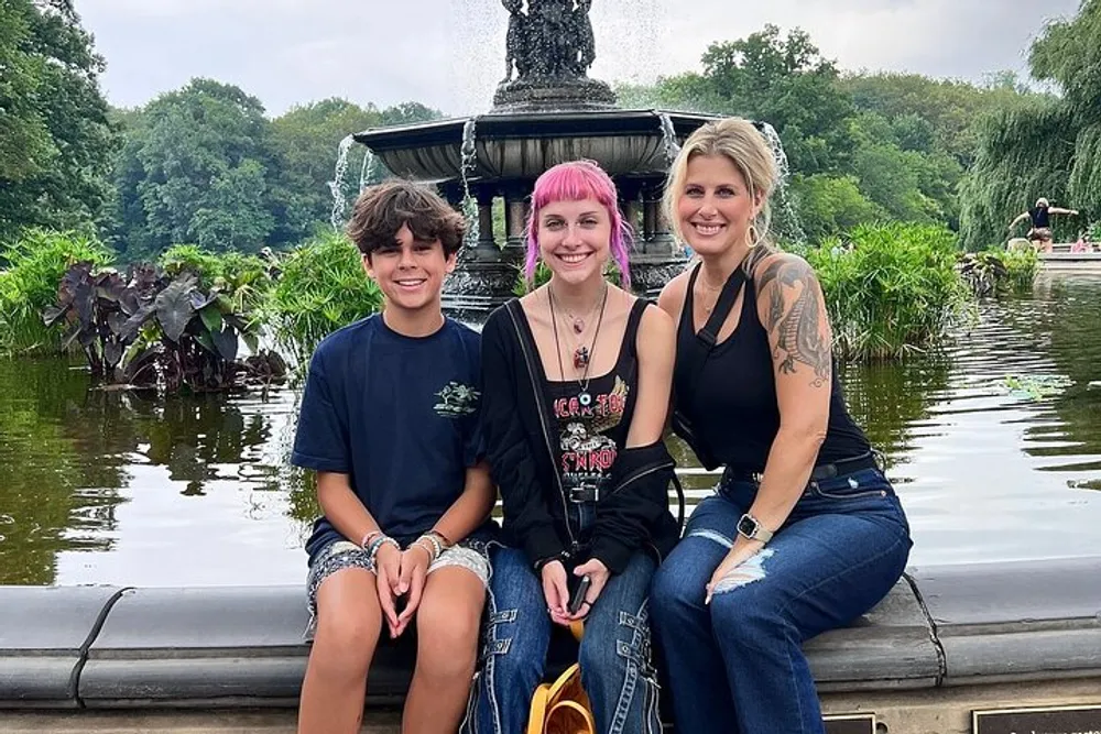 Three people are smiling for a photo in front of a fountain and pond surrounded by lush greenery