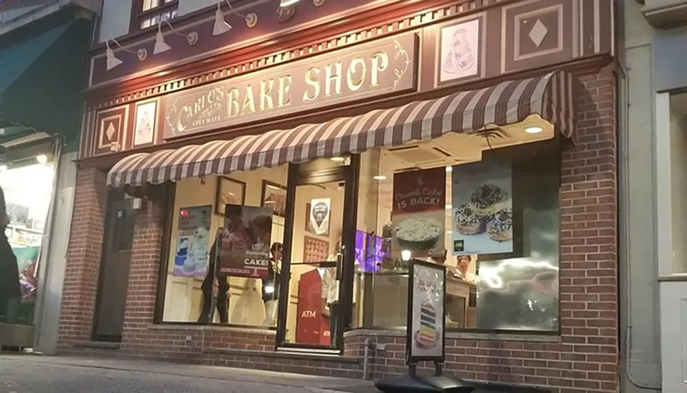 The image shows the storefront of Carloss Bake Shop at dusk adorned with striped awnings and displaying signs for cakes and an ATM inside