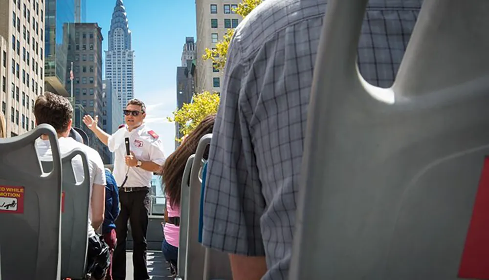 A guide is enthusiastically speaking to passengers on what appears to be a city tour bus with the urban backdrop suggesting it might be in a busy metropolitan area