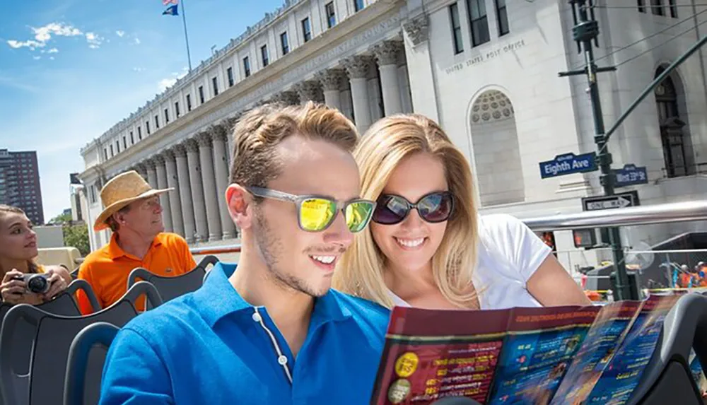 A couple is smiling and looking at a brochure together while sightseeing on a double-decker tour bus in a city