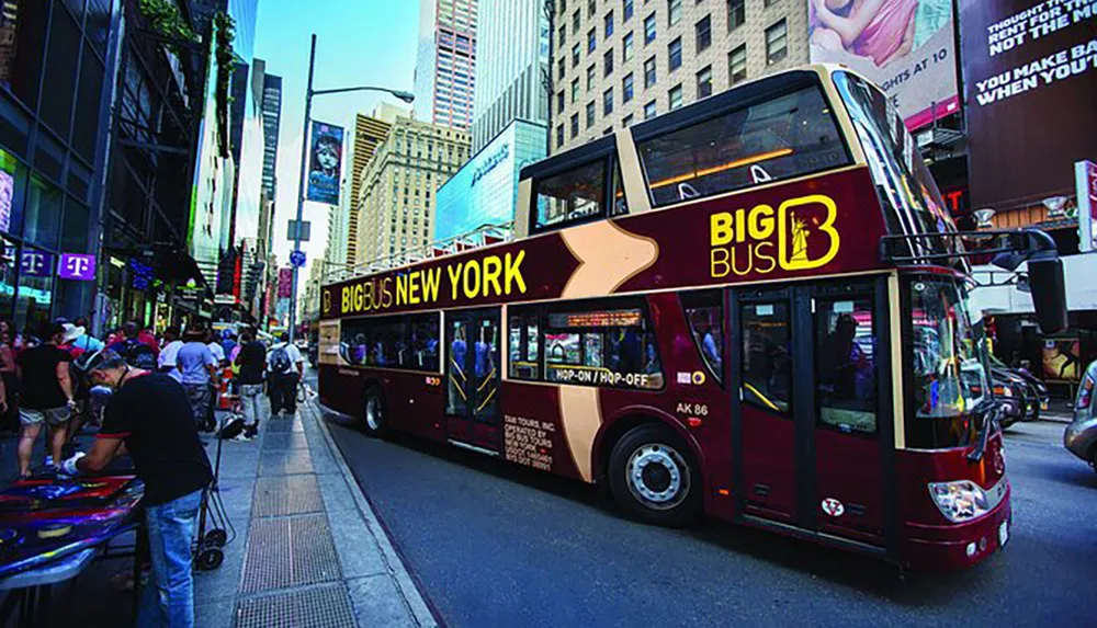 A double-decker Big Bus New York tour bus is navigating through a busy urban street with pedestrians and towering skyscrapers