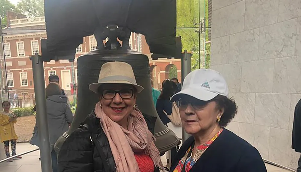 Two women are posing for a photo in front of the Liberty Bell in Philadelphia