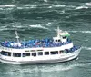 A crowded tour boat filled with passengers wearing blue ponchos is navigating a rippled body of water