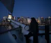 A person is gazing at the city skyline at dusk from the deck of a sailing boat
