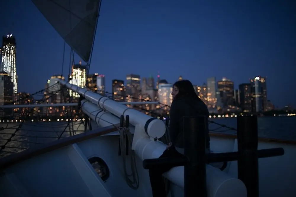 A person leans on the railing of a boat enjoying the view of a city skyline at dusk