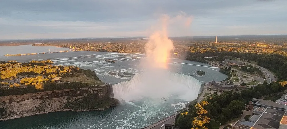 The image captures a majestic aerial view of Niagara Falls bathed in golden sunlight with mist rising above the cascading waters