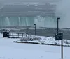 The image shows the misty and mighty Niagara Falls during a cloudy day with snow and ice along its banks