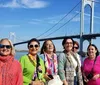 A group of smiling women poses in front of a suspension bridge on a sunny day