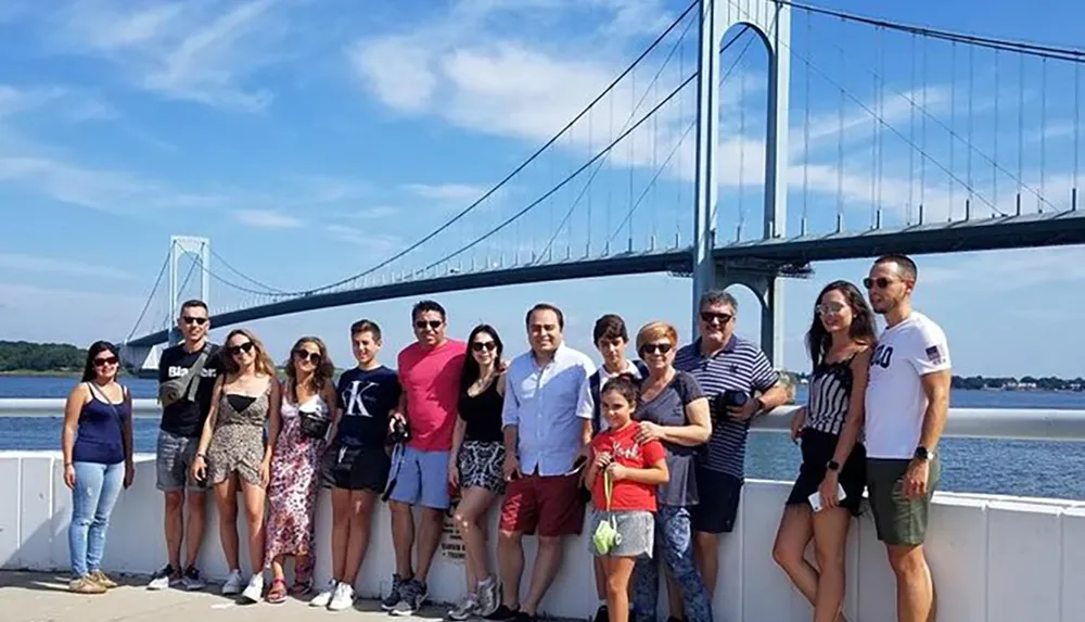 A group of people is posing for a photo in front of a large suspension bridge on a sunny day