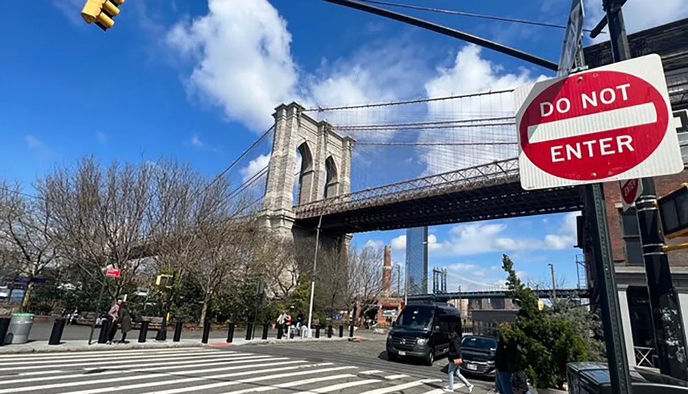 The image features an urban street scene with a DO NOT ENTER sign in the foreground and a view of the Brooklyn Bridge against a blue sky with scattered clouds in the background