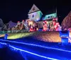 A house is vibrantly decorated with colorful Christmas lights and festive inflatable decorations including Santa Claus and candy canes creating a cheerful nighttime holiday scene