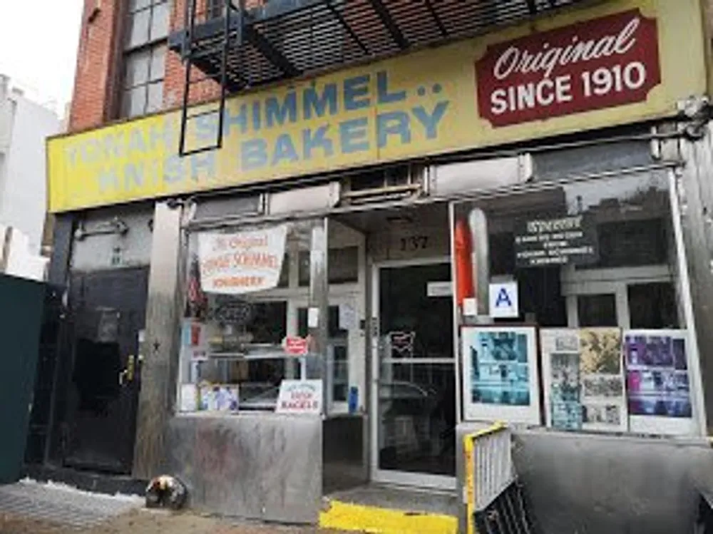 The image shows an old-fashioned bakery storefront with signage indicating it has been operating since 1910 and it has a health grade A displayed on the window