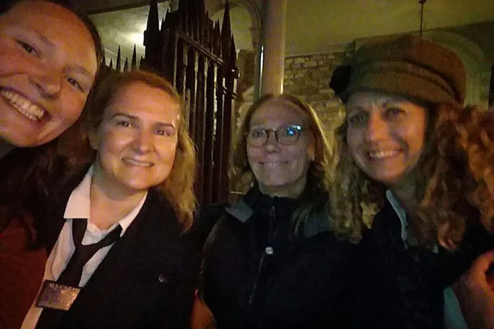 Four people are smiling and posing for a selfie at night time with what appears to be a fence and a building in the background