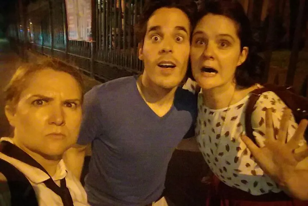 Three people are posing with exaggerated expressions of surprise or shock for a selfie at night