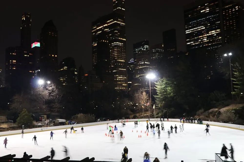 Skaters enjoy an evening on an outdoor ice rink with the illuminated backdrop of a city skyline