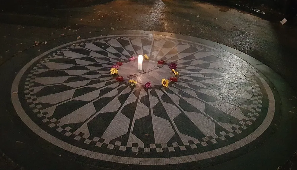 The image shows a mosaic with the word IMAGINE at its center surrounded by a few flowers and a lit candle possibly a tribute or memorial